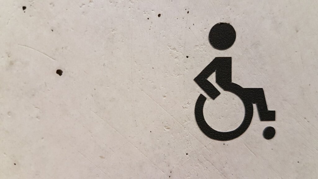 black spray painted disability sign on a white concrete wall 